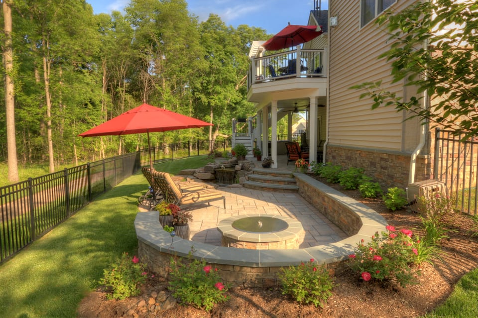 Backyard paver patio with curved seating wall around fire pit by Deckscapes of Virginia