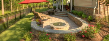 Backyard paver patio with curved seating wall around fire pit by Deckscapes of Virginia