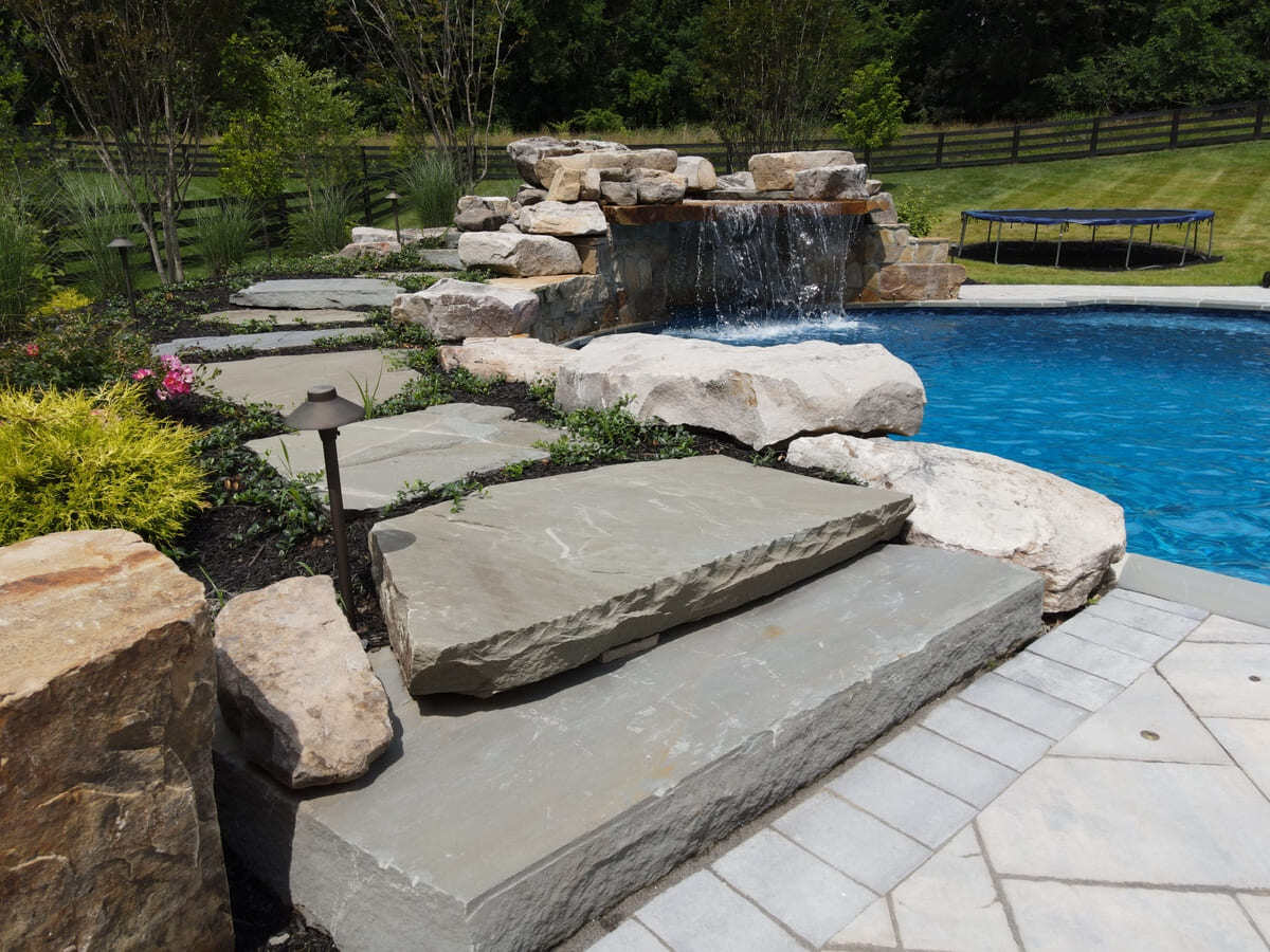 Northern Virginia pool area with stone steps and waterfall by Deckscapes of VA