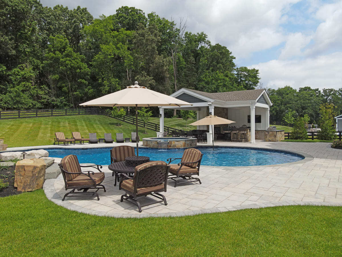 Paver patio with outdoor furniture next to freeform pool by Deckscapes of Virginia