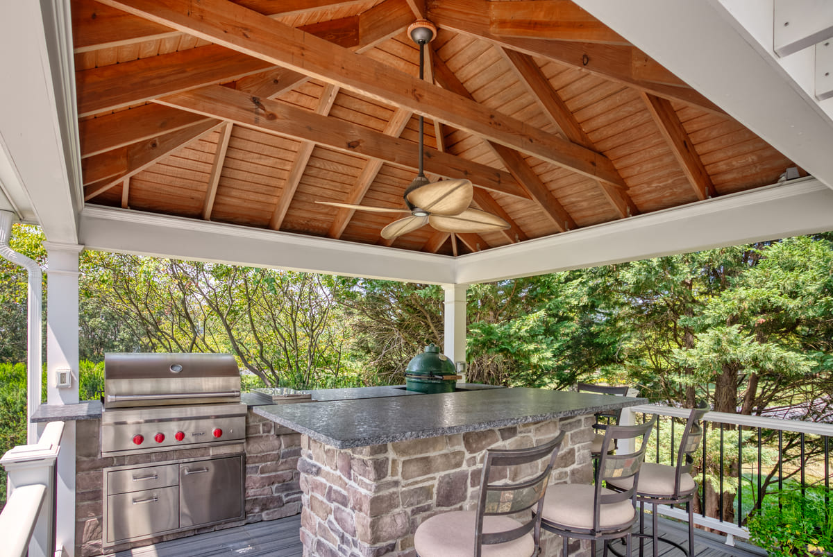 Covered outdoor kitchen with island, grill, and smoker below ceiling fan on deck by Deckscapes of VA
