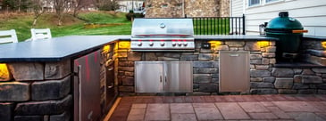 Custom-built outdoor kitchen with grill and smoker at dusk with task lighting on