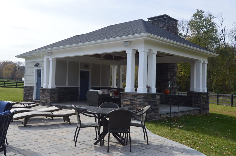 Patio and pool house exterior with stone veneers and white posts by Deckscapes of Virginia