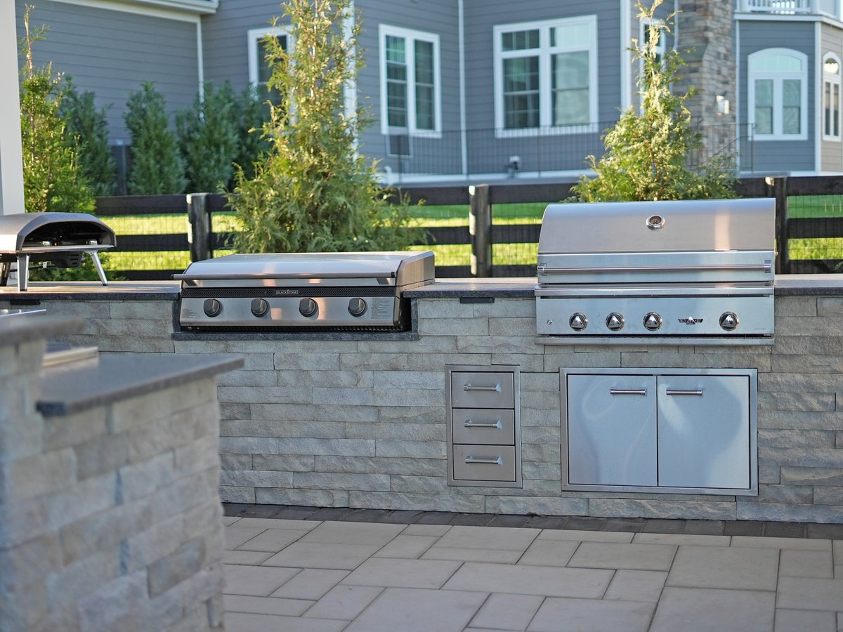 Outdoor kitchen with tan stone, grill, smoker, and storage by Deckscapes in Northern VA