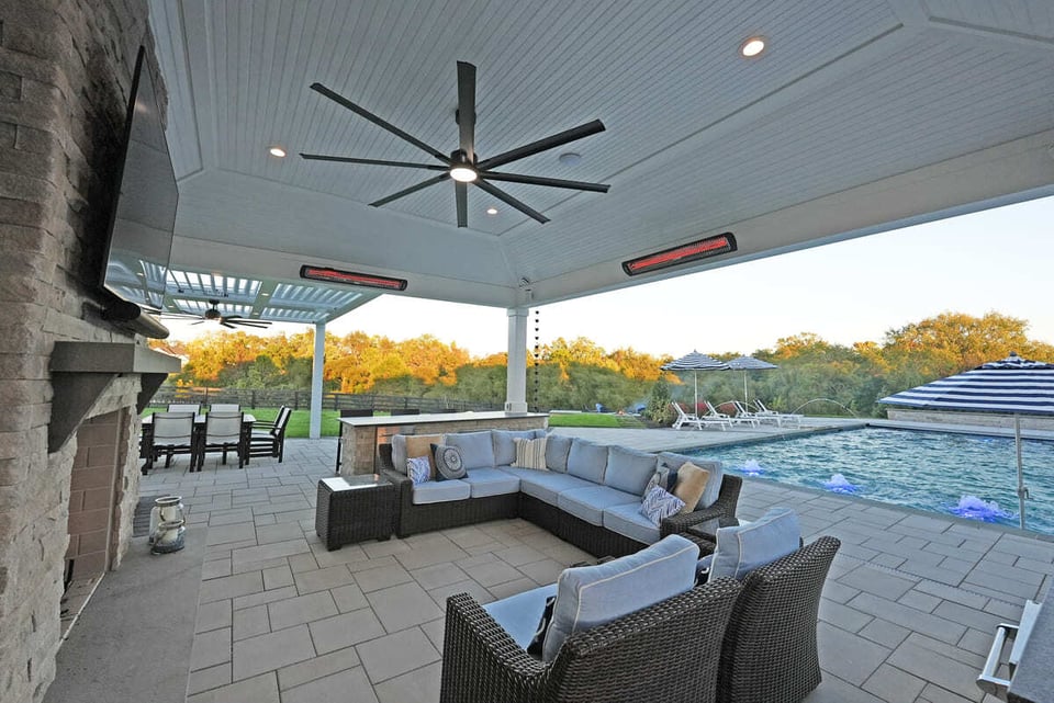 Covered patio with heaters, fan, and fireplace, with seating and TV in VA by Dekscapes