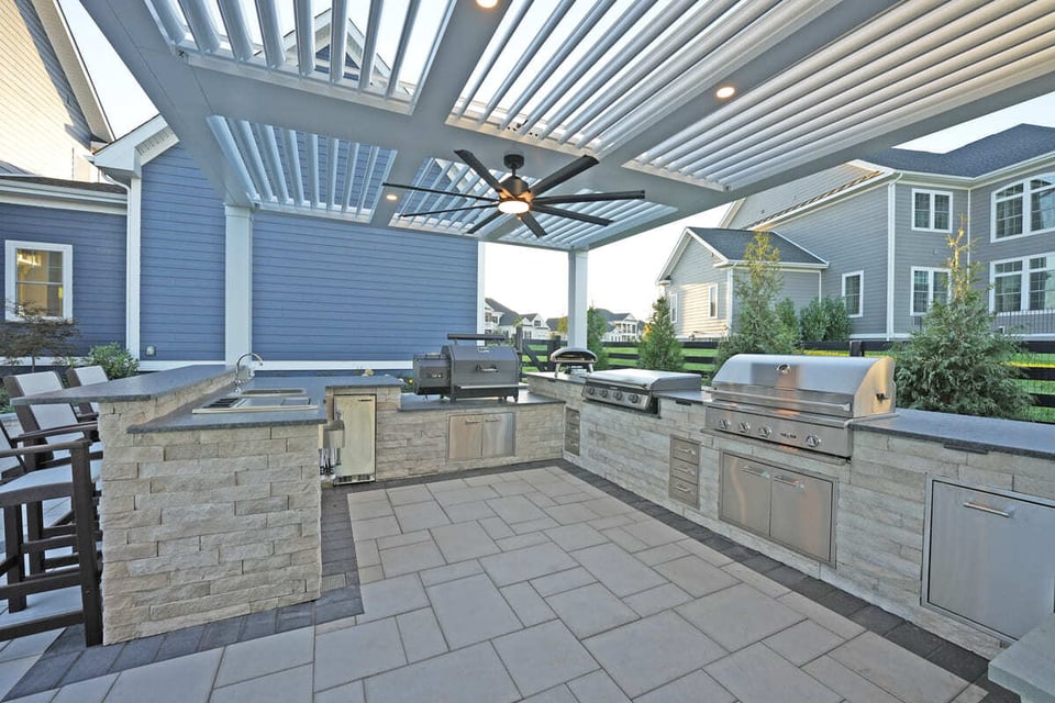 outdoor kitchen in Virginia under a slated pergola featuring grill, smoker, pizza oven, storage, and sink
