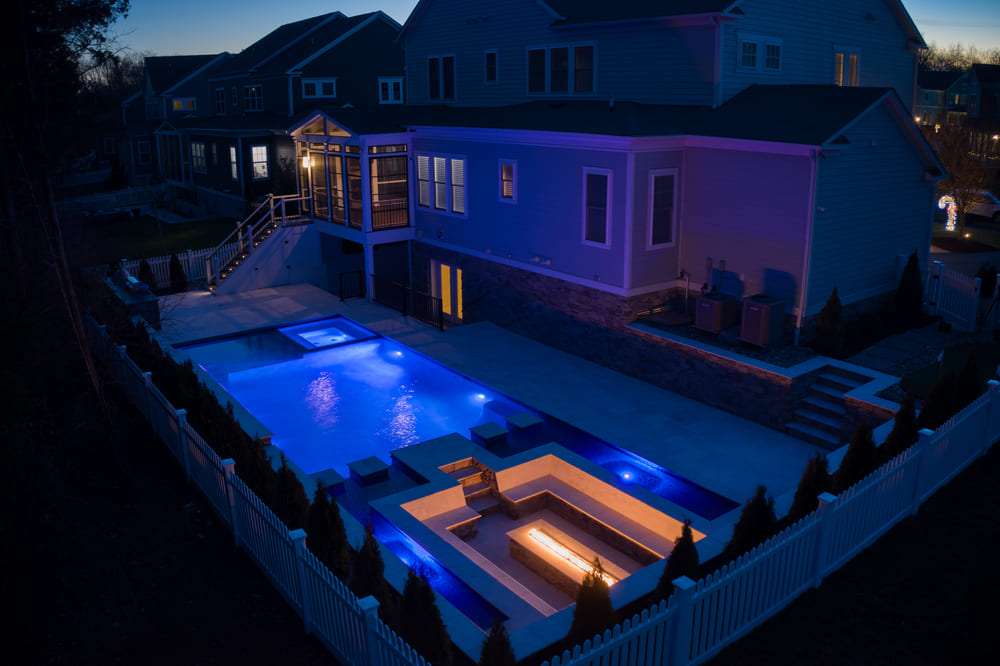 Drone view of Northern Virginia backyard at night with luxury gunite pool and porch by Deckscapes of VA