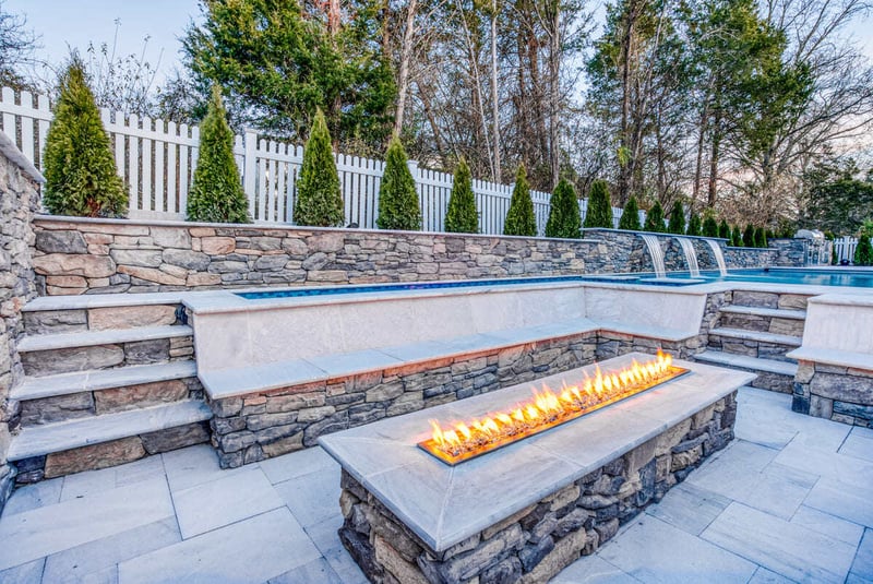 Evergreens along fence of gunite pool and seating area by Deckscapes of VA