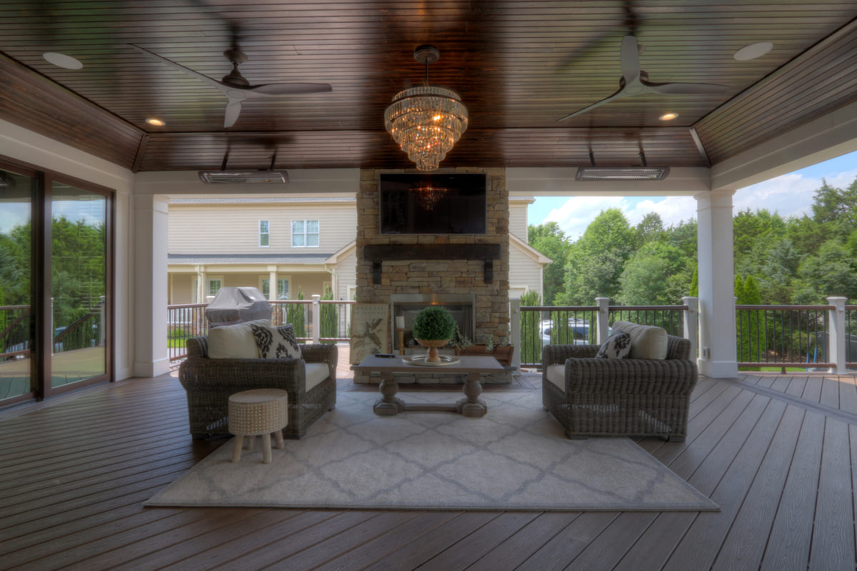 Fireplace on covered deck with two ceiling fans and heaters above by Deckscapes of Virginia