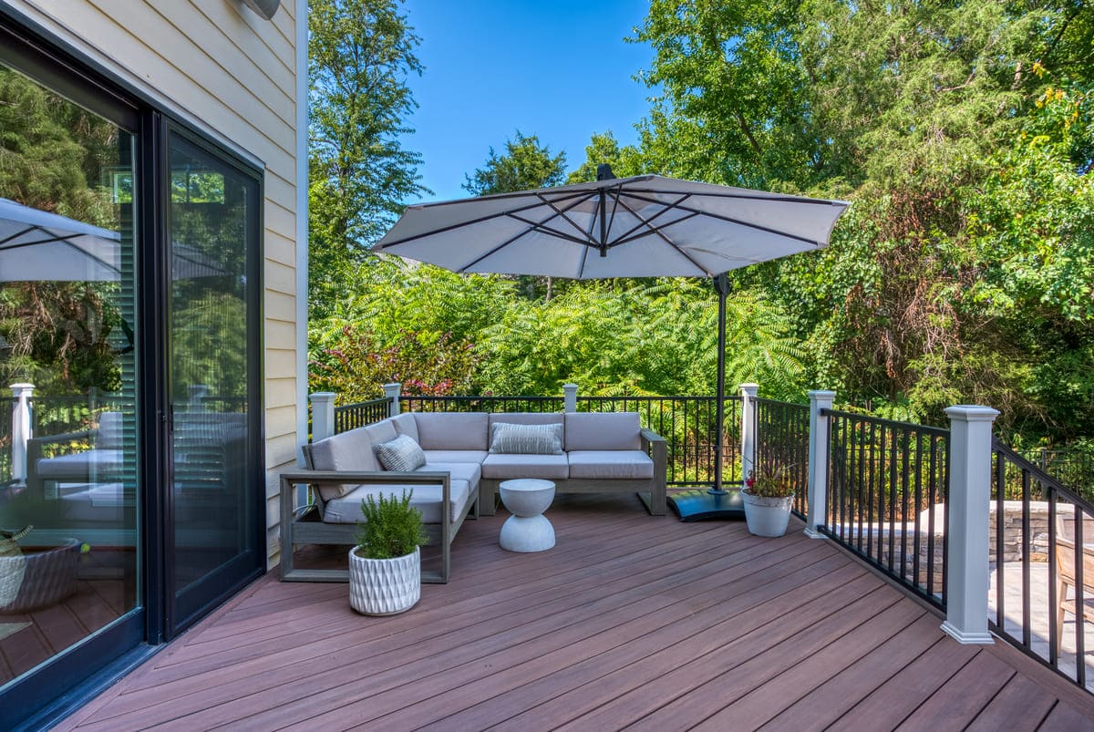 Deck with cushioned sectional and umbrella by Deckscapes of VA