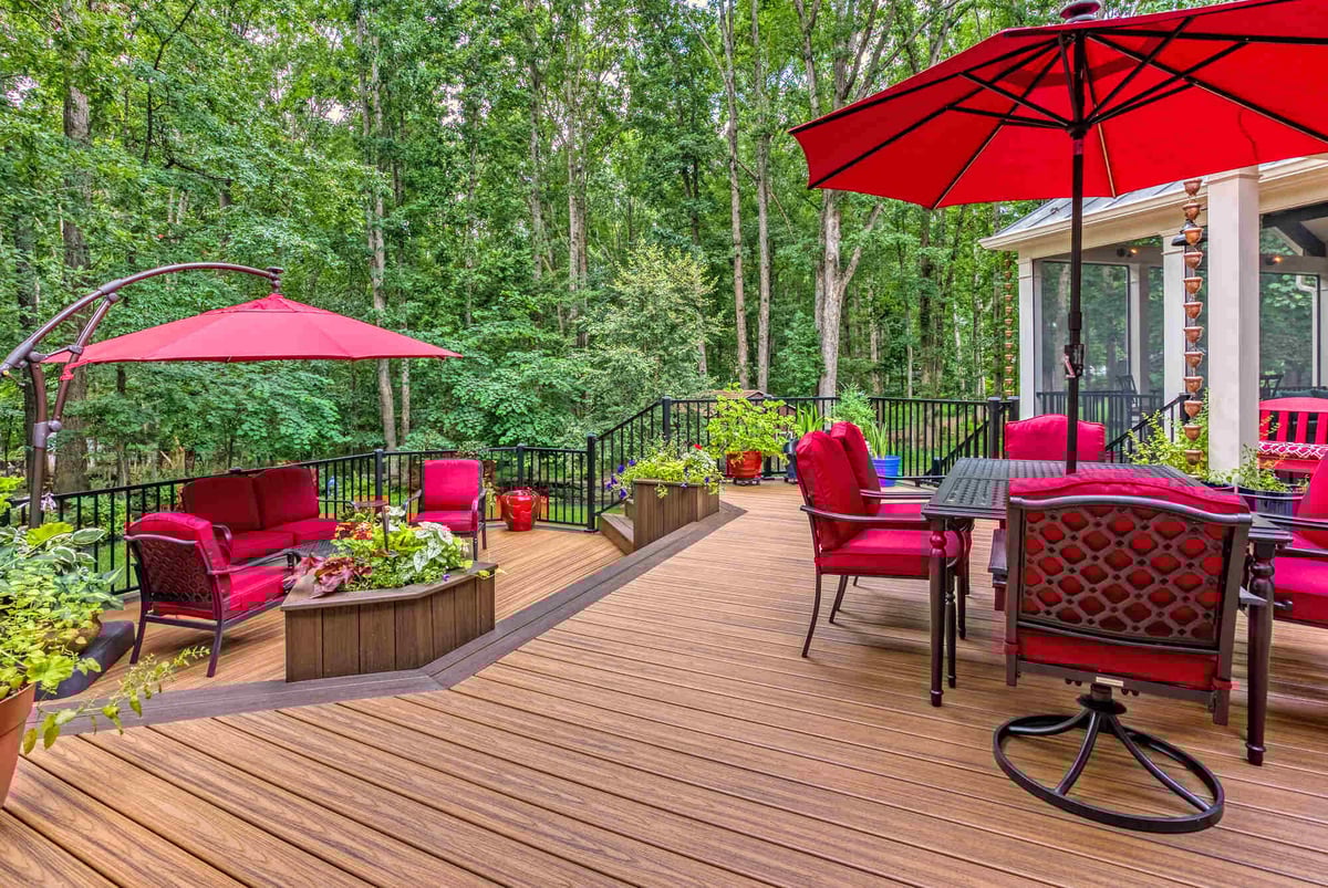 Red outdoor furniture and umbrella with potted plants on patio by Deckscapes of Virginia