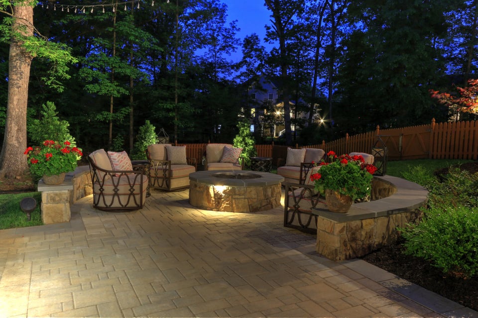 Round patio at night with fireplace and curved retaining wall by Deckscapes of VA