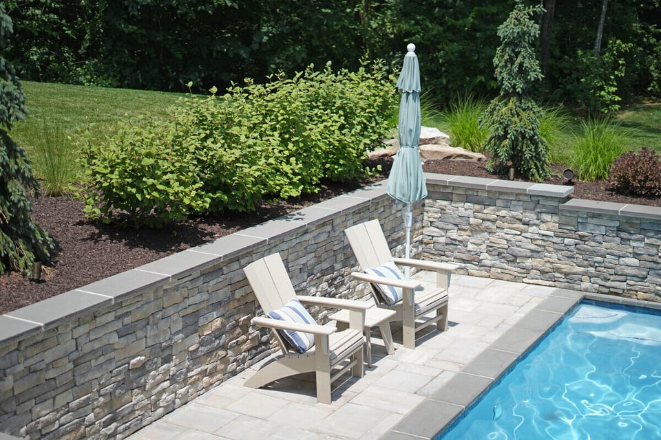 Two chairs on poolside patio with stacked stone wall design by Deckscapes of VA