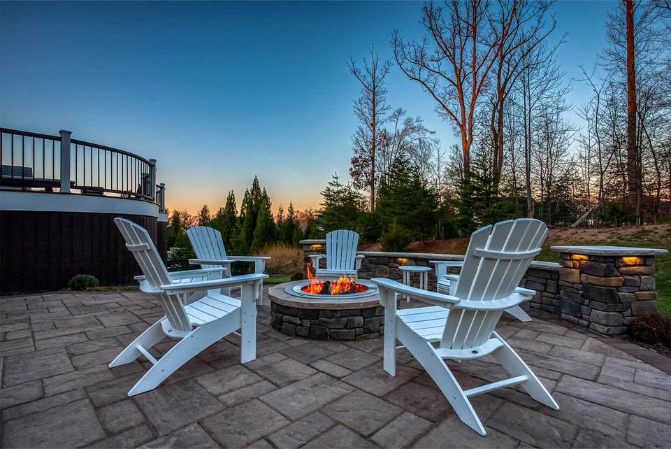 Cozy fire pit area with white Adirondack chairs and stone patio set by Deckscapes of Virginia