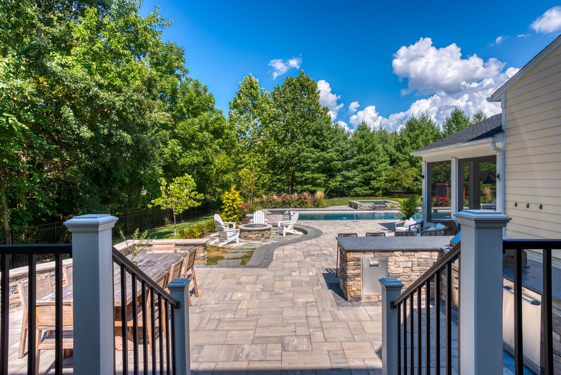 Large backyard patio from deck stairs with outdoor kitchen, fire pit, and seating wall by Deckscapes of VA