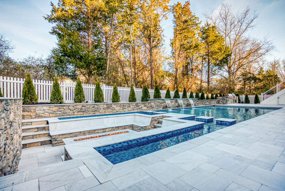 Marble paver steps going down rectangular fire pit with built-in seating area by gunite pool 