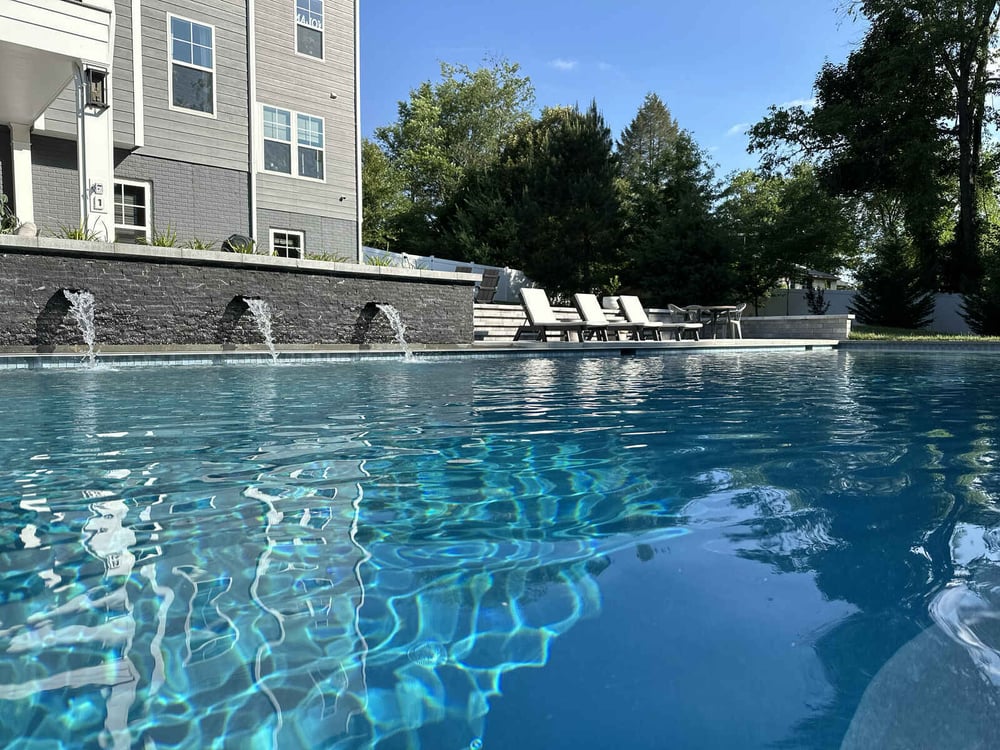 Modern backyard pool with waterfall feature and lounge chairs, created by Deckscapes of Virginia