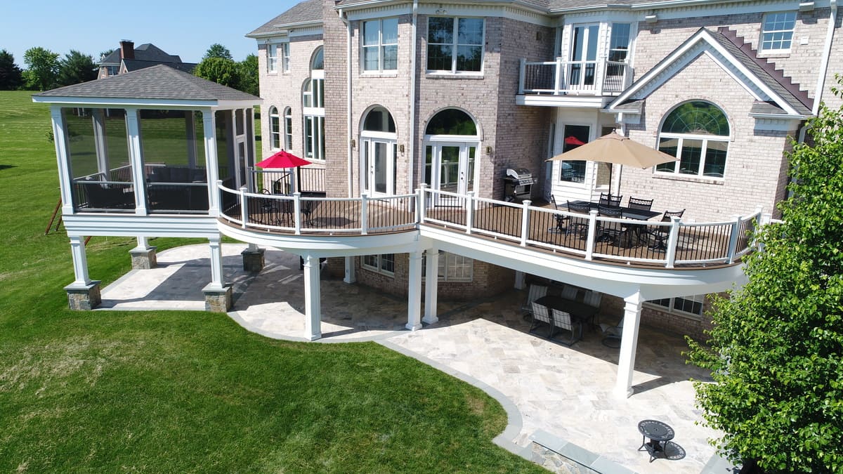 Multi-level deck and screened-in porch with curved railings on flat landscape by Deckscapes of Virginia