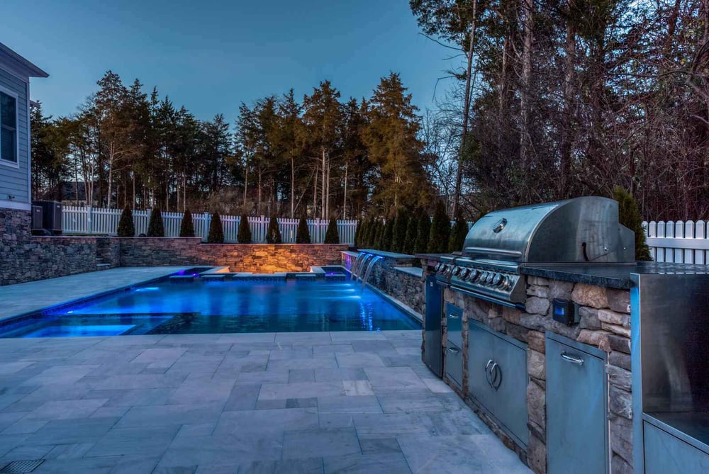 Northern VA backyard with stone and night pool with lights and waterfall by Deckscapes
