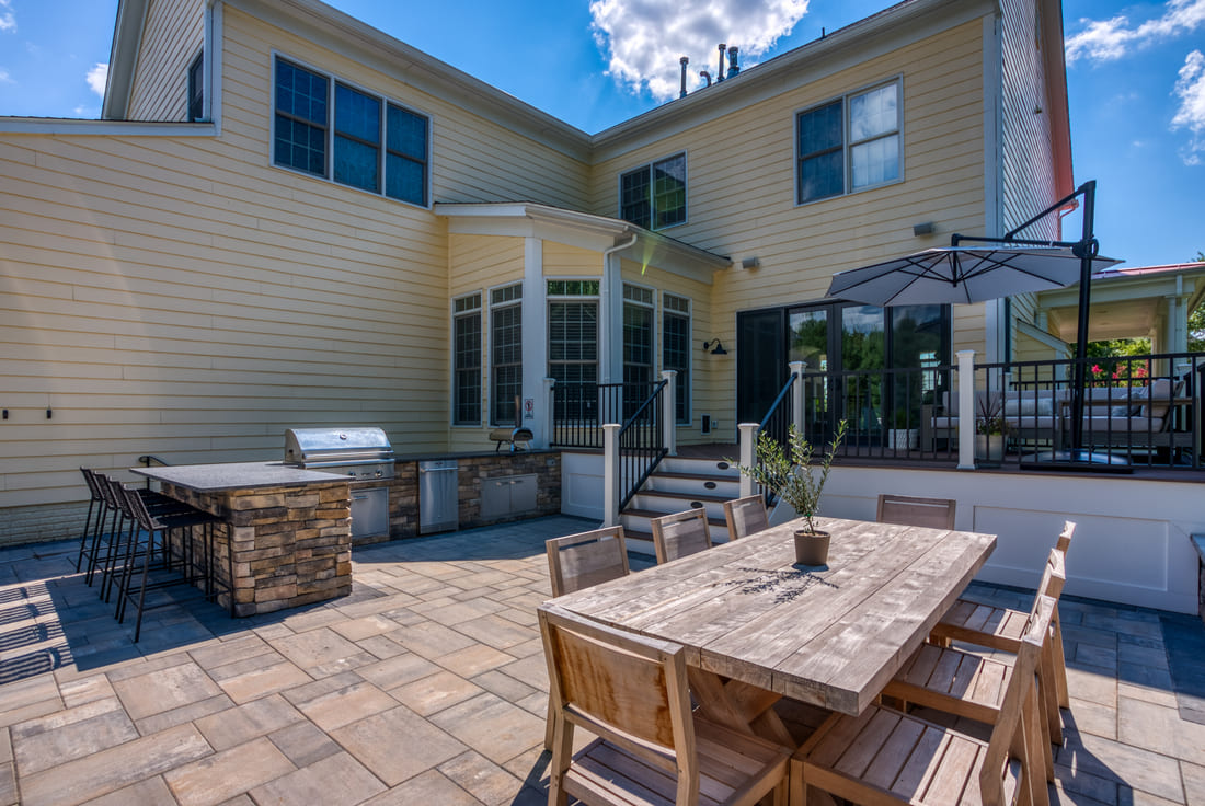 Outdoor kitchen on backyard patio with steps leading to deck in Northern Virginia