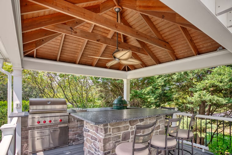 Outdoor kitchen with custom-built shade structure and ceiling fan above seating area