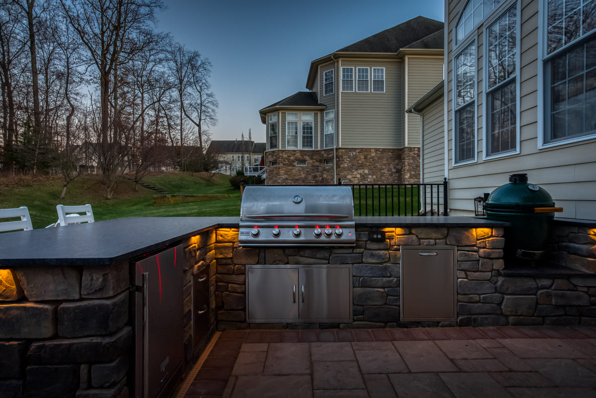 Outdoor kitchen with grill, smoker, and custom lighting by Deckscapes of Virginia