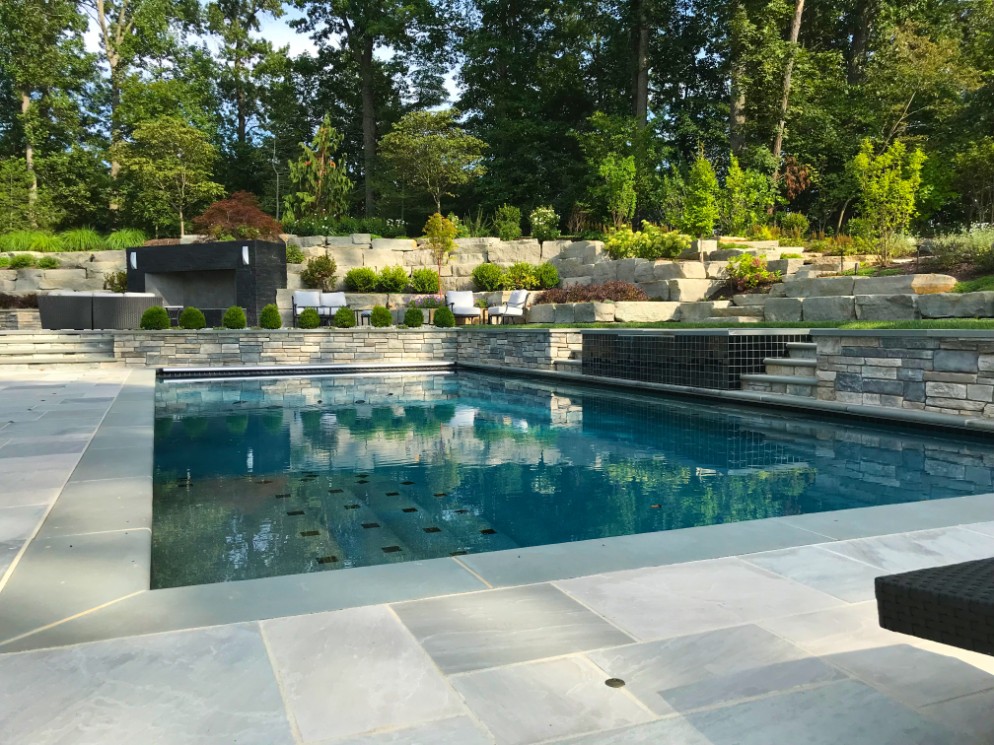 Gunite pool with patio and stone retaining wall in back by Deckscapes of Virginia