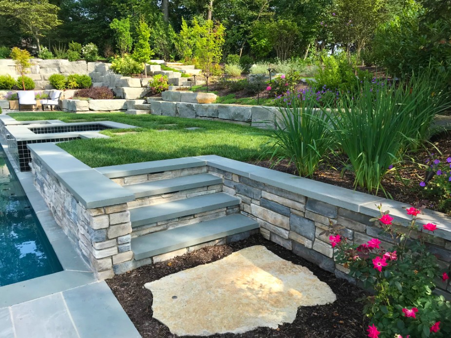 Stone steps and landscaping next to pool on sunny day by Deckscapes of Virginia