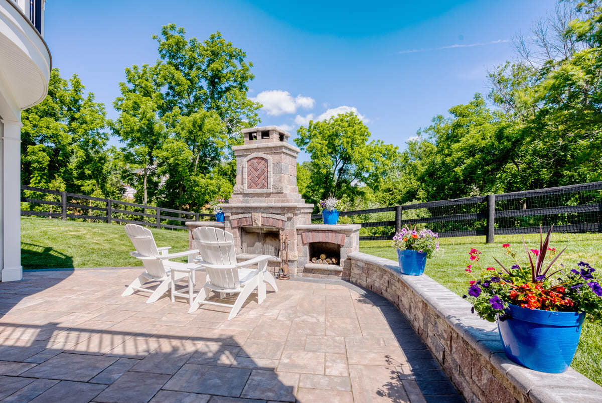 Paver patio with outdoor furniture and custom fireplace with log storage by Deckscapes of VA