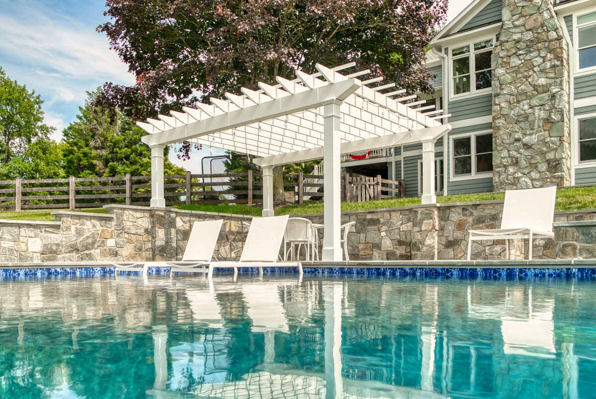 Pergola and chairs on tanning ledge of gunite pool by Deckscapes of Virginia