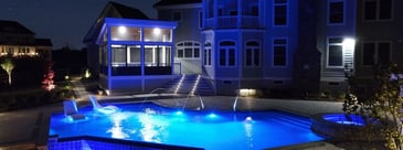 Pool, patio, and porch at night with custom lighting and waterfall features by Deckscapes of Virginia