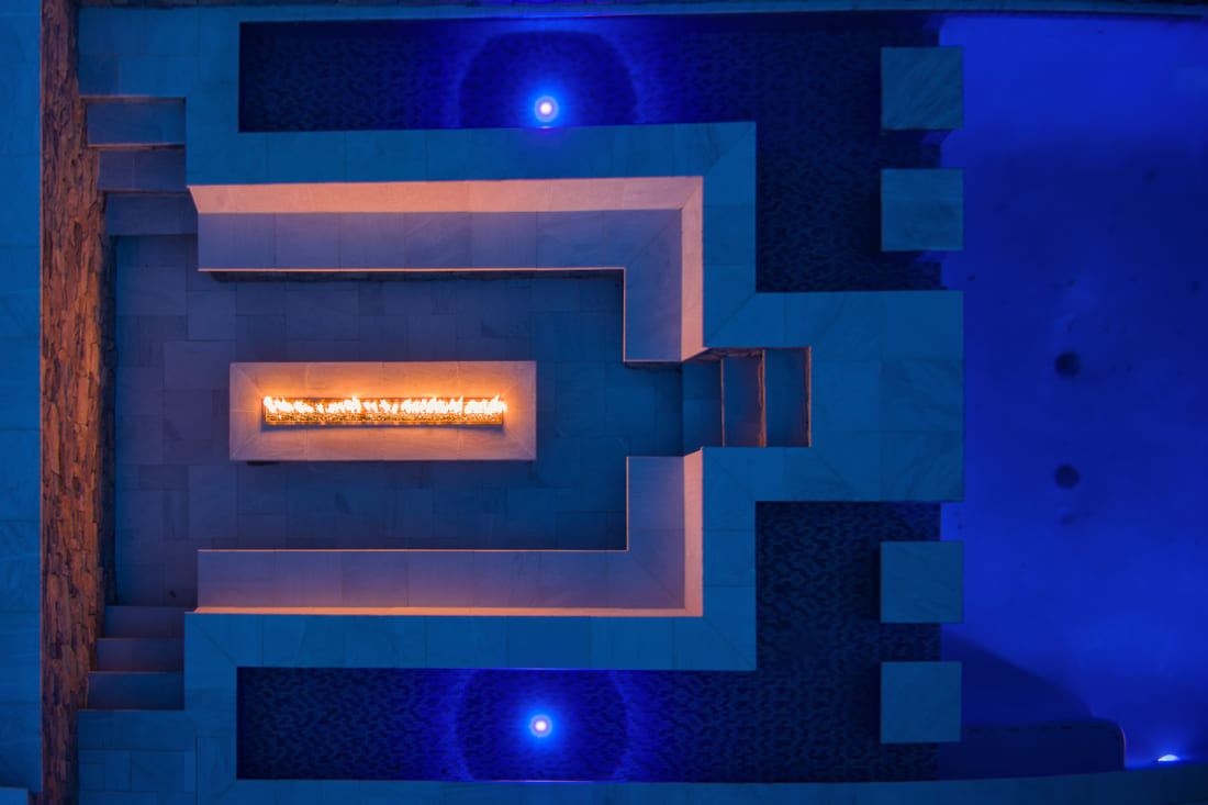 Rectangular fire pit in stone seating area next to in-ground gunite pool at night by Deckscapes of VA Rectangular fire pit in stone seating area next to in-ground gunite pool at night by Deckscapes of VA