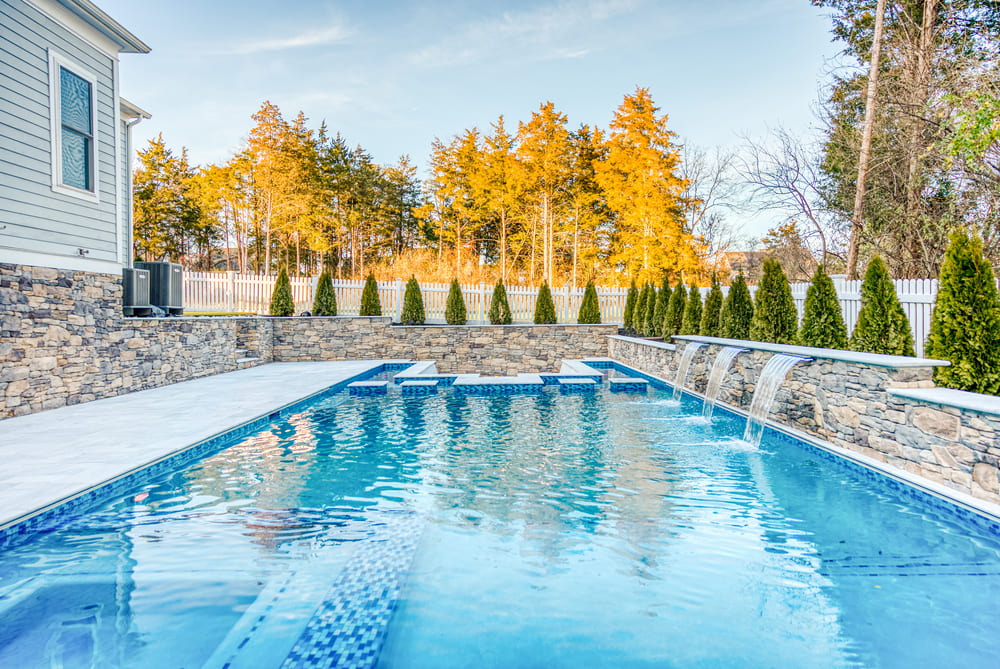 Rectangular gunite pool with stone waterfall feature by Deckscapes of Virginia