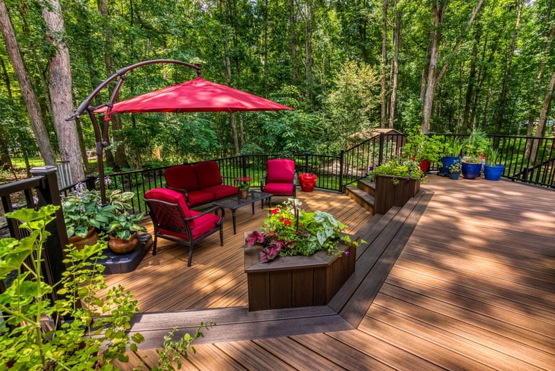 Red outdoor furniture and umbrella with potted plants on patio by Deckscapes of Virginia