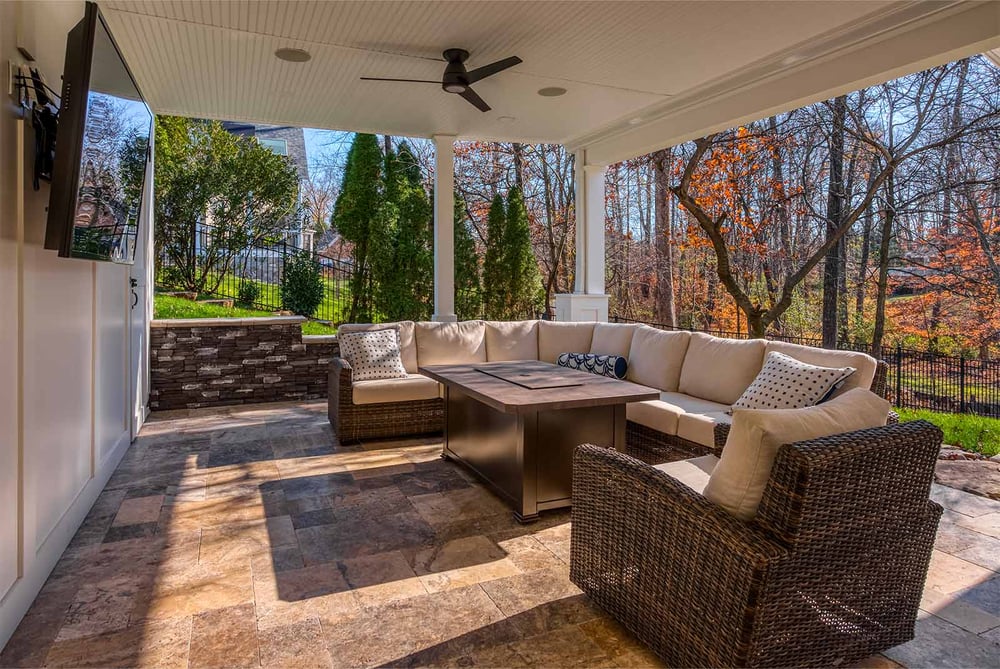 Covered patio with ceiling fan, TV, wicker sectional, and fire table by Deckscapes of Virginia