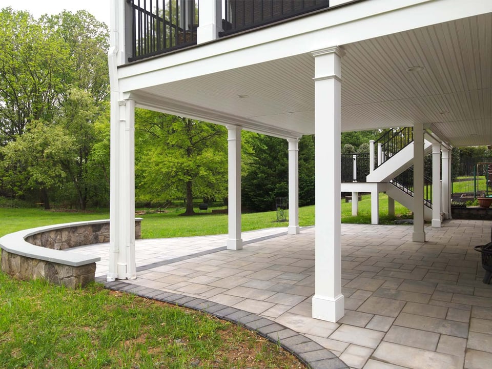 Covered patio with paver flooring in Northern Virginia backyard under second-story deck