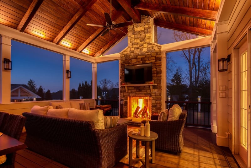 Screened-in porch night time with fireplace floating tv and ceiling fans at night