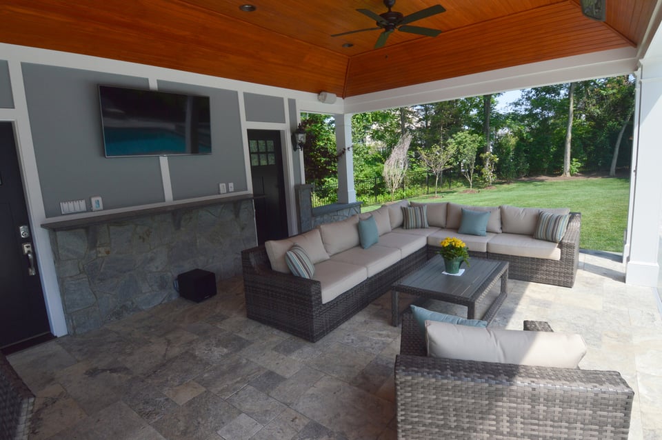 Covered porch of a pool house in outdoor remodeling project in Northern VA by Deckscapes with seating, heater, fan, and TV