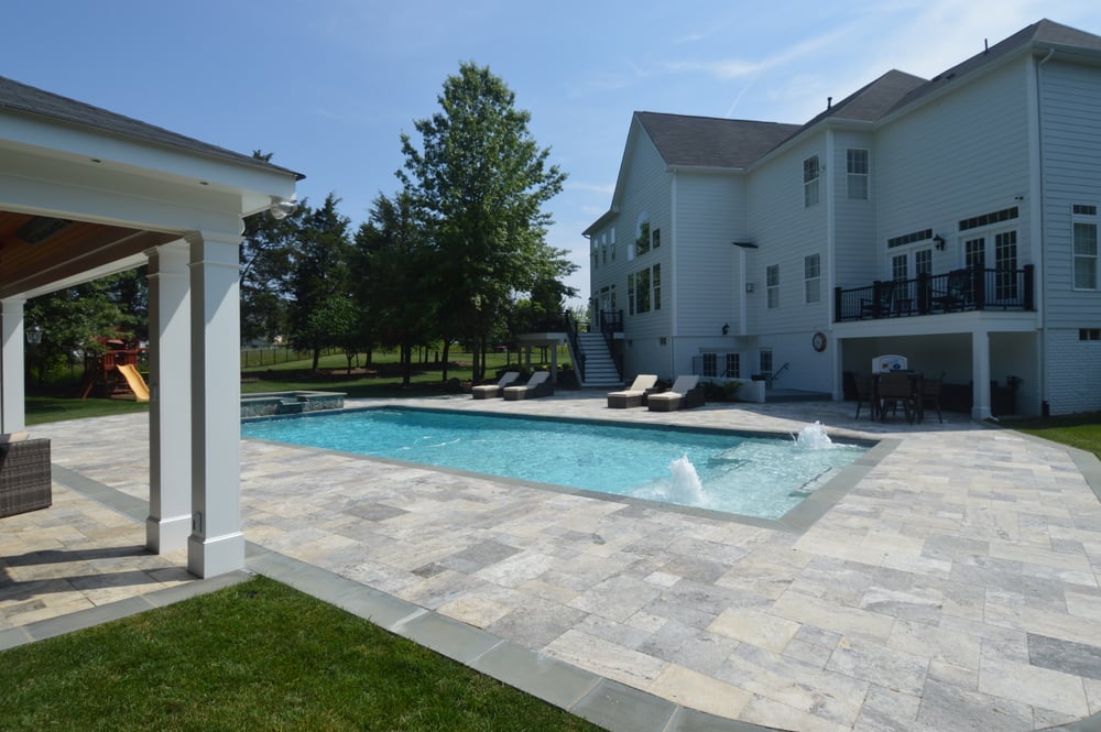 Pool with fountains next to custom patio in outdoor remodeling project by Deckscapes of Virginia