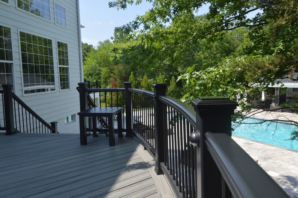 View over black curved second-level composite deck railing of pool and patio below in Northern VA