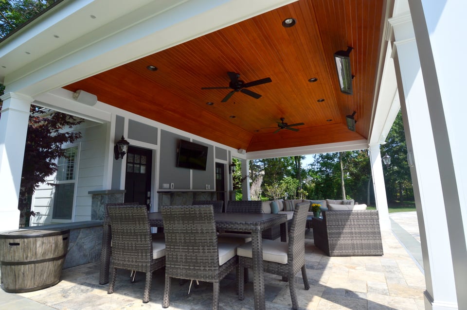 Seating area of covered porch with fan, heaters, custom lighting next to a pool in Northern VA by Deckscapes of Virginia