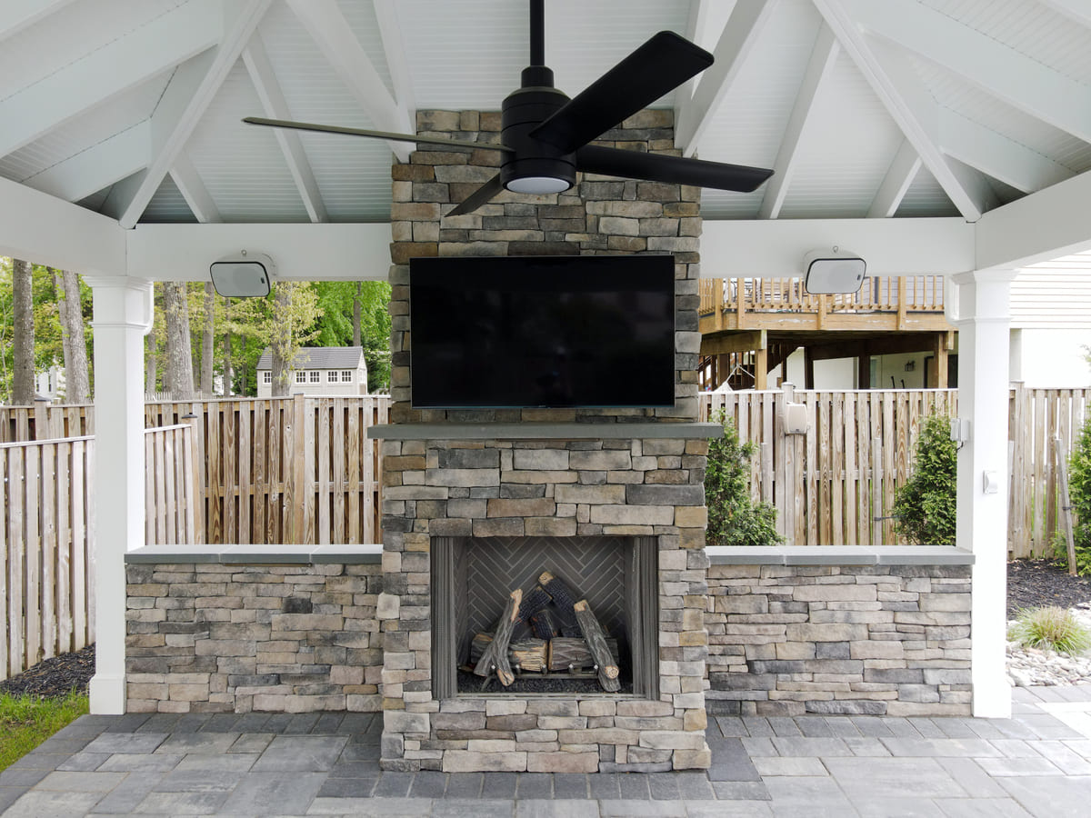 Stone veneer fireplace with TV above mantle in pool pavilion by Deckscapes of VA