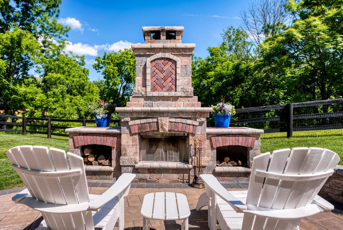 Two Adirondack chairs in front oof brick and stone fireplace on patio by Deckscapes of Virginia