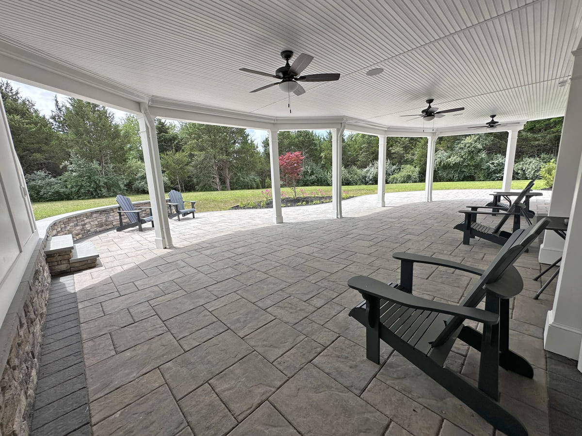 Underdeck living space with three ceiling fans above and curved retaining wall by Deckscapes of Virginia