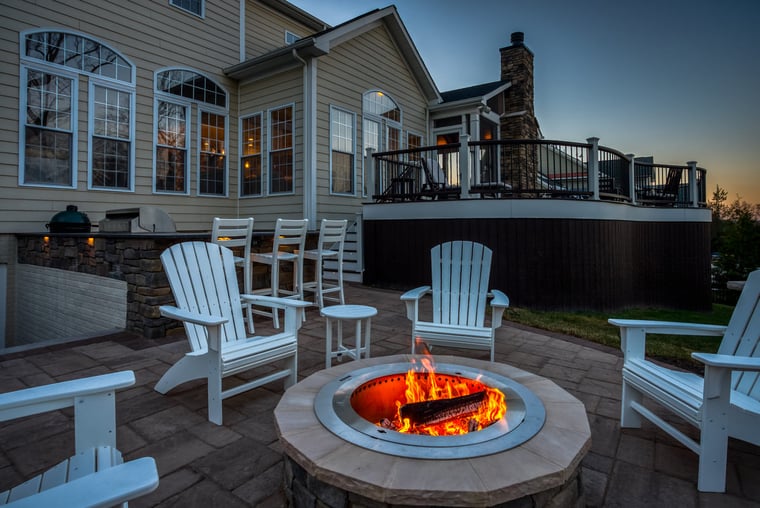 Patio at dusk with chairs around stone fireplace and outdoor kitchen