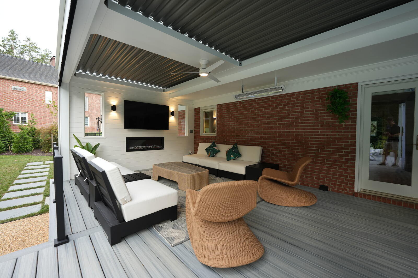 Cozy covered patio featuring modern furniture and a mounted TV, designed by Deckscapes of Virginia