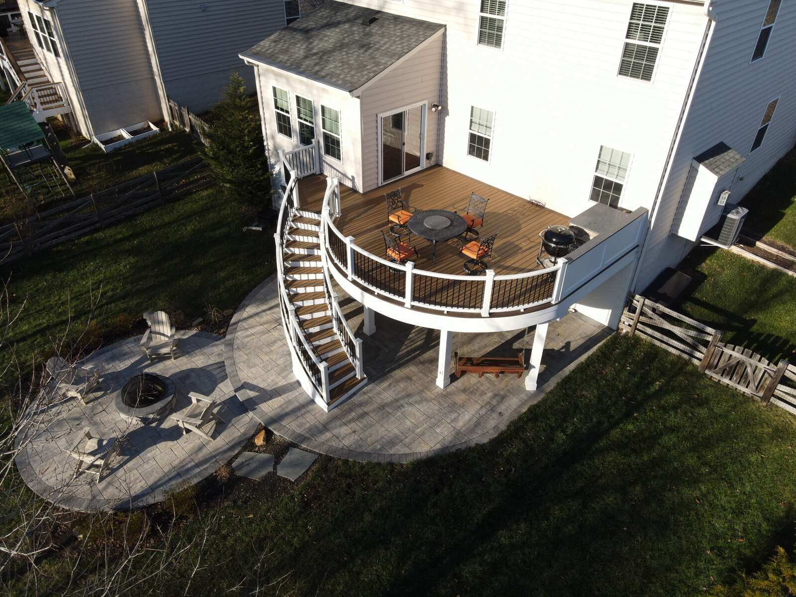 Elevated deck with curved staircase and patio featuring a fire pit, designed by Deckscapes of Virginia