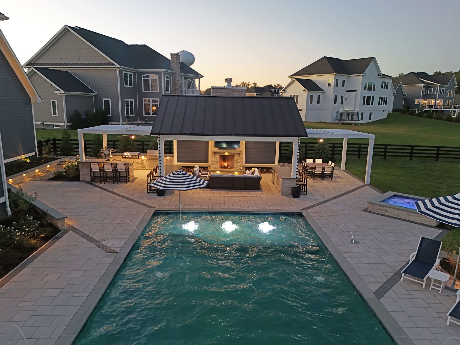 Drone view of pool house and pool at twilight with custom lighting by Deckscapes of VA