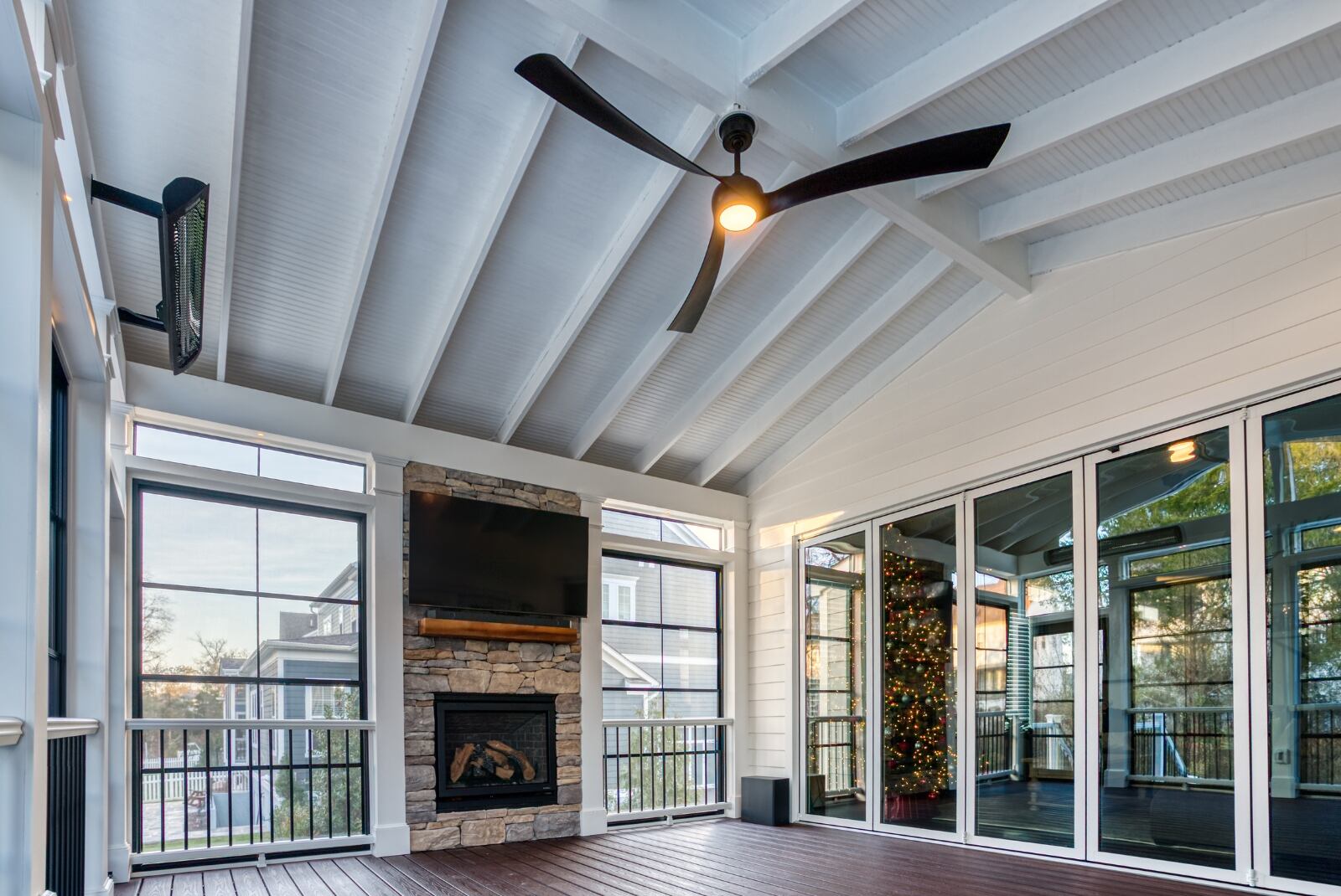 Screened-in porch with floating tv and stone fireplace below ceiling fan and Bromic heater