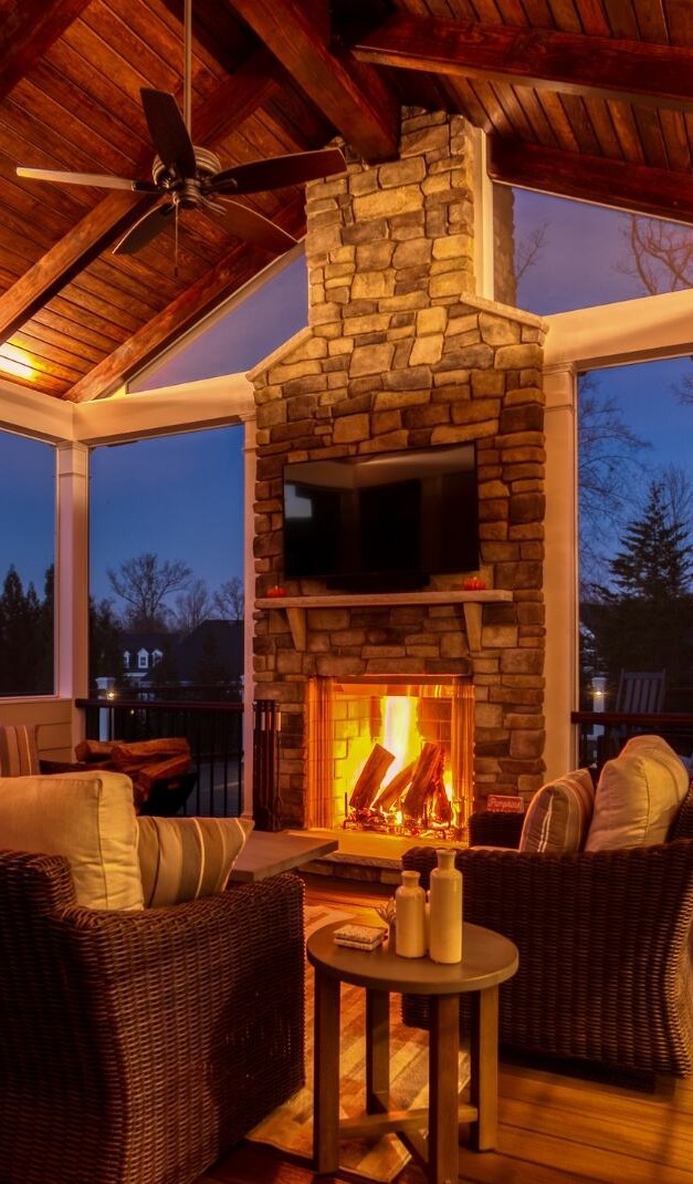 screened in porch night time with fireplace floating tv and ceiling fans at night